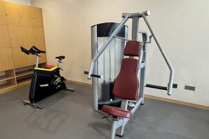 A gym with a stationary bike, a red exercise bench, and a wall-mounted exercise machine.
