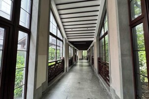 A corridor with large windows on both sides, a tiled floor, and a wooden ceiling.