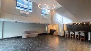 Un intérieur spacieux avec un plafond haut, un coin salon, un comptoir d’accueil et un luminaire moderne.
