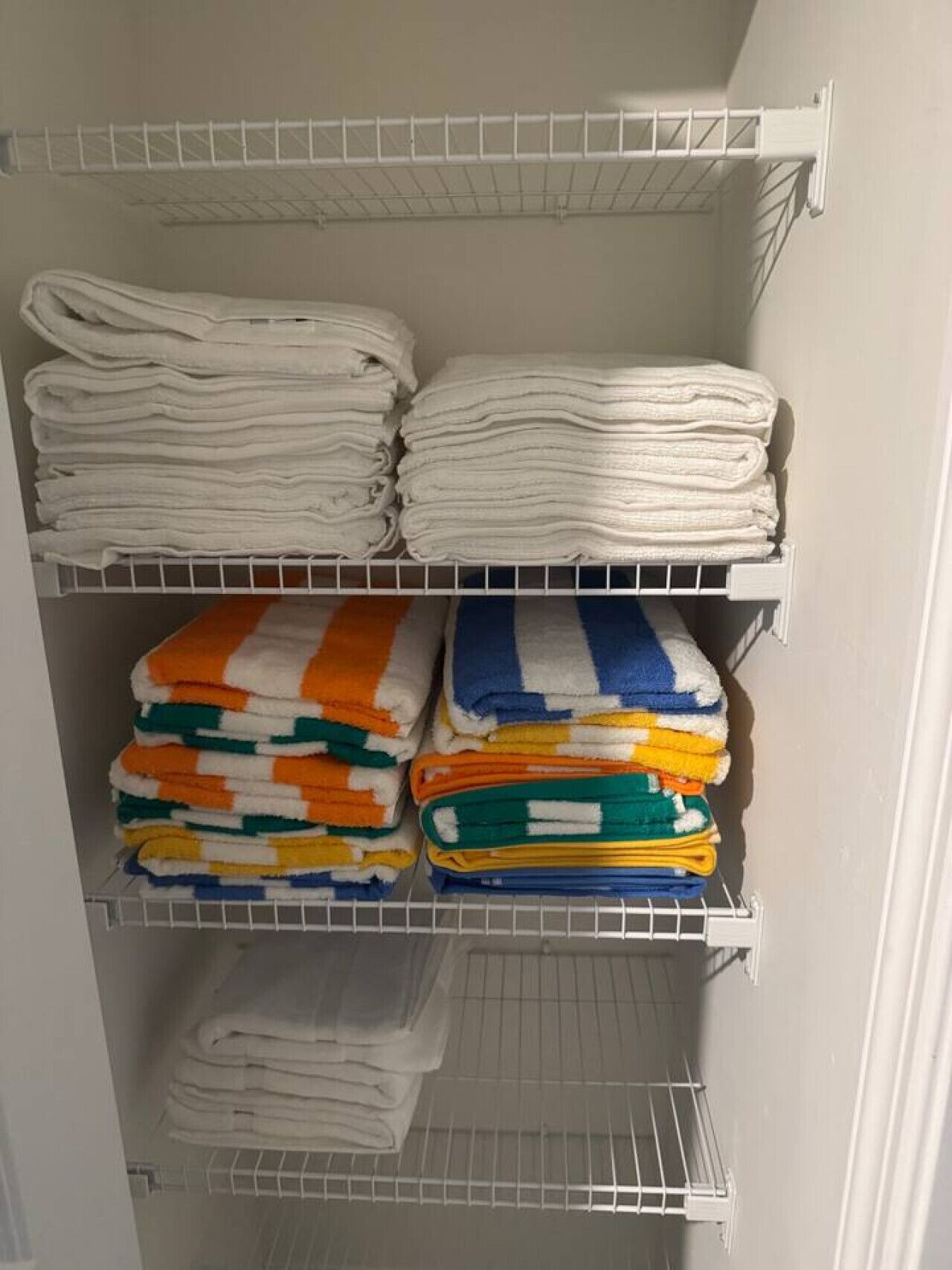 Ett förvaringsutrymme med hyllor där hopvikta handdukar i färgerna vitt, orange, grönt och blått förvaras.