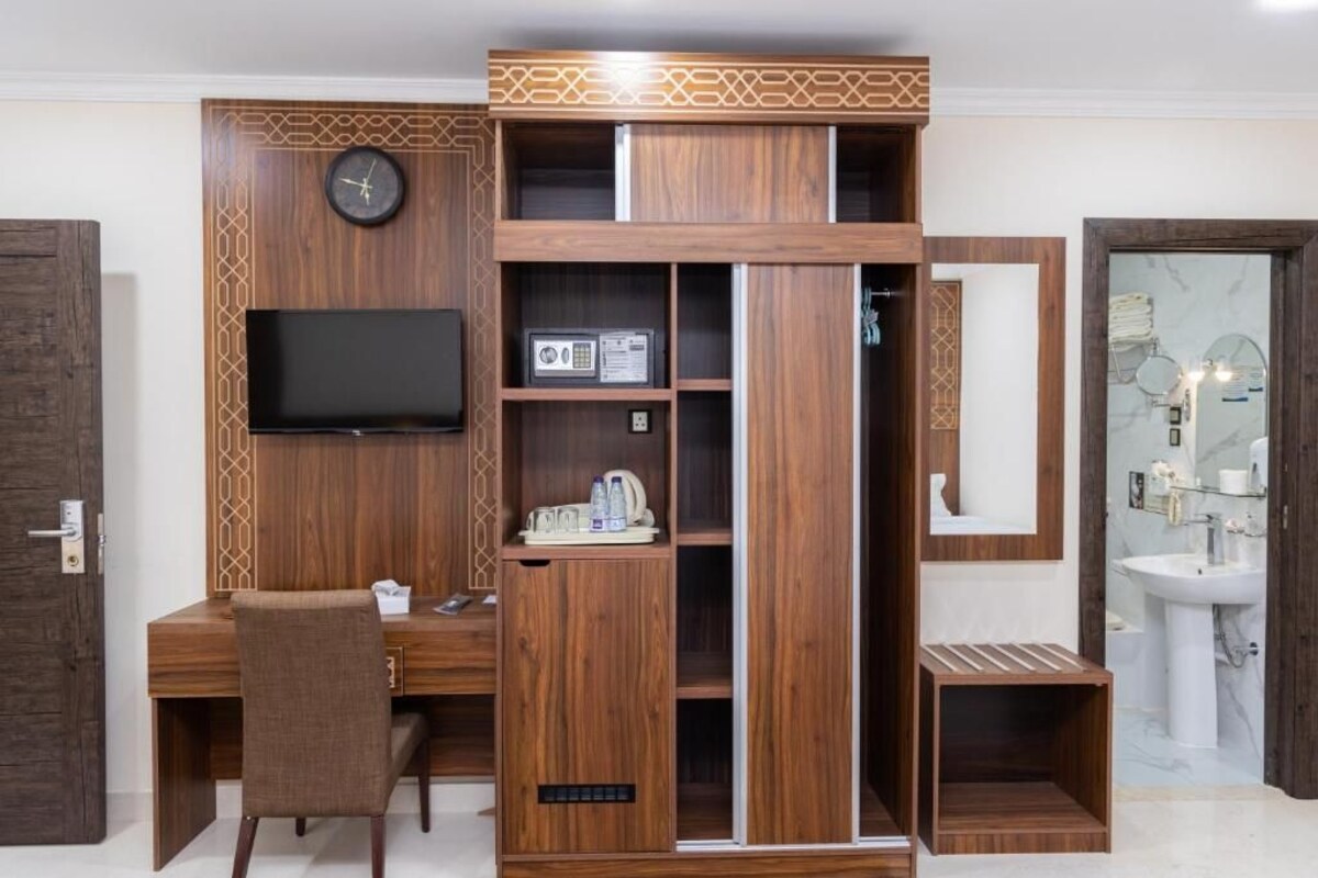 A modern room with a wooden desk, a television, a clock, and a bathroom with a sink and mirror.