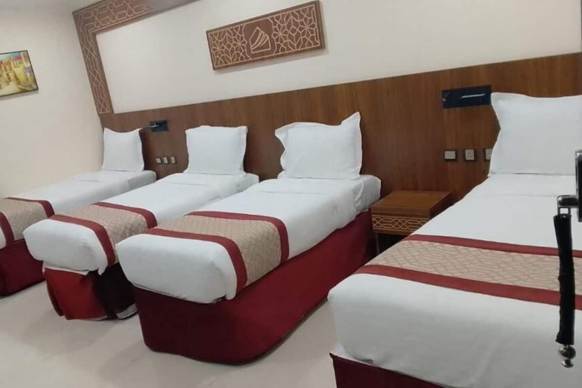 A hotel room with four beds arranged in a row, a wooden headboard, and a wall-mounted artwork.