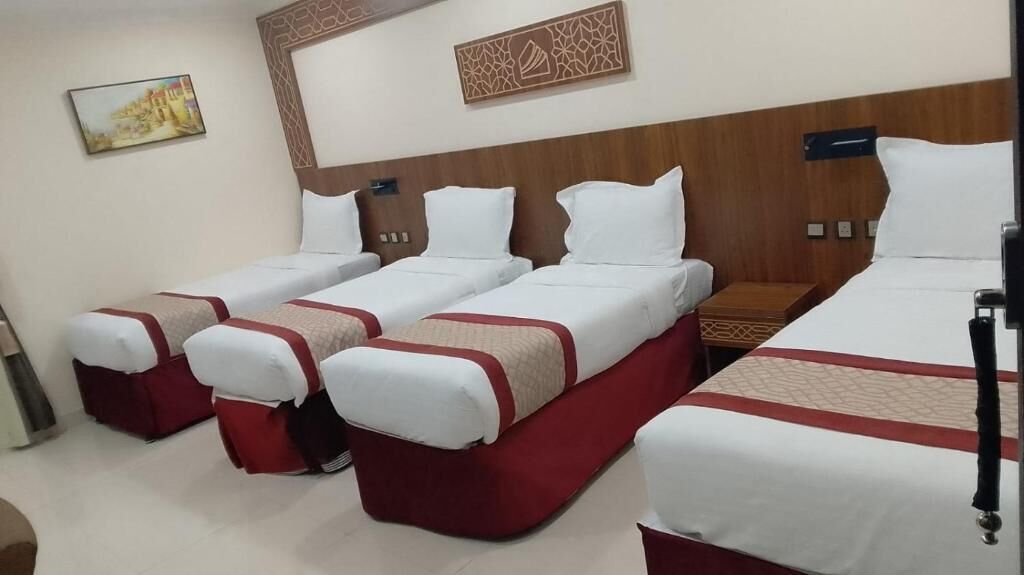 A hotel room with four beds arranged in a row, a wooden headboard, and a wall-mounted artwork.