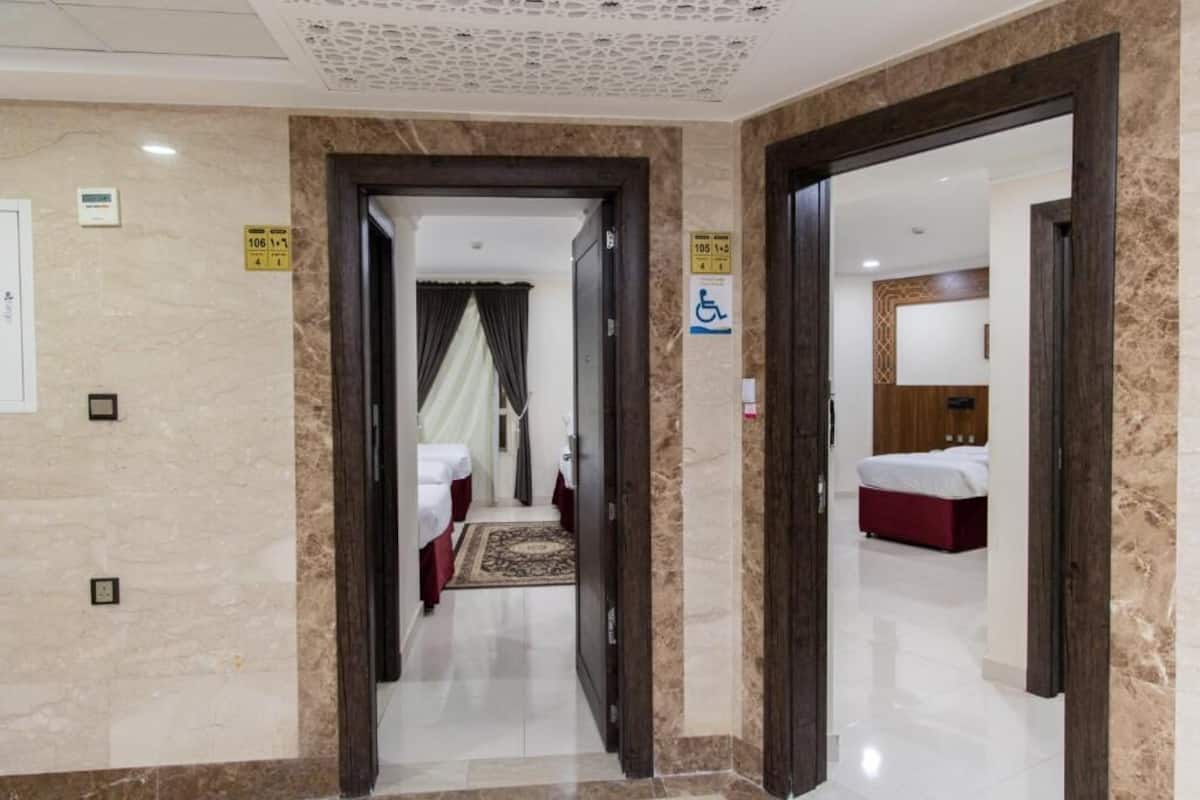 A hotel corridor with a carpeted floor, a bed with a red headboard, and a wheelchair-accessible sign.