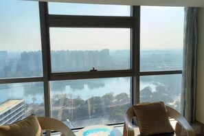 A room with large windows, two chairs, and a view of a cityscape and water. - Fusion International Garden Apartment（Qingpu Branch Of Zhongshan Hospital） (Shanghai)