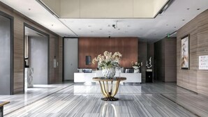 Un vestíbulo moderno con suelo de mármol, un mostrador de recepción y una mesa decorada con flores.