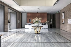 A modern lobby with a marble floor, a reception desk, and a decorative table with flowers.