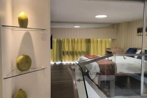 A hotel room with a glass partition, a bed, a sofa, and a small table.