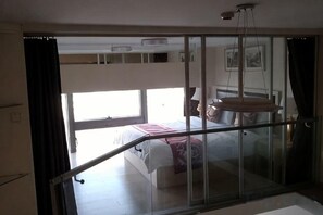 Een slaapkamer met een bed, een raam en een balkon met een hekwerk.