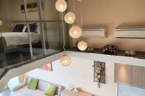 Una moderna camera d'albergo con parete in vetro, un divano, un comodino e una lampada a sospensione.