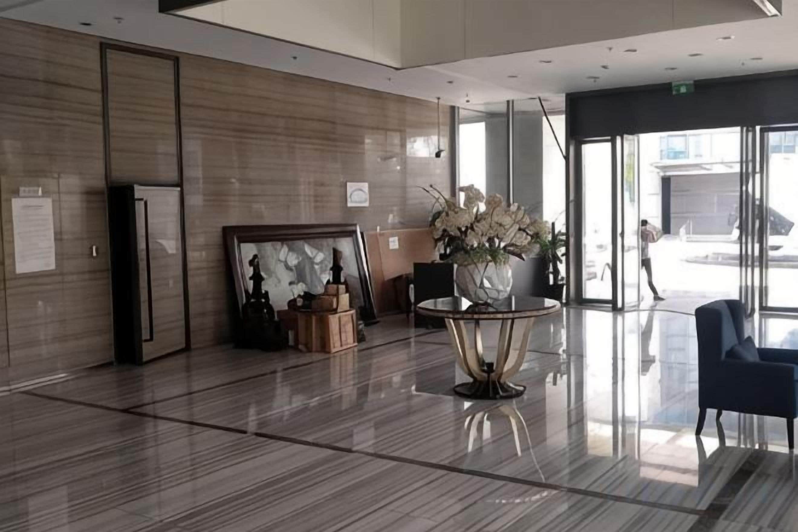 A modern lobby with a polished floor, framed artwork, a vase with flowers, and a seating area.