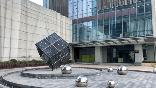 Un edificio moderno con fachada de vidrio, una escultura cúbica negra grande y varias esculturas esféricas en una plaza circular.