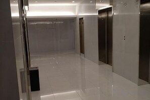 Een moderne liftruimte met een glanzende vloer, een glazen deur en een bedieningspaneel voor de lift aan de muur.