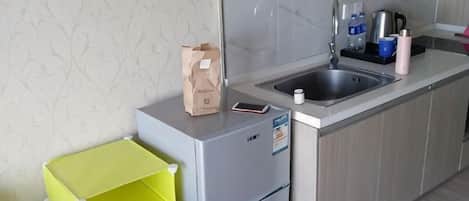 Una cocina con refrigerador, pileta y encimera con una bolsa de pan y una botella.