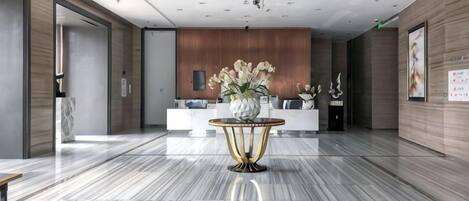 A hotel lobby with a reception desk, a marble floor, and a decorative table with flowers.