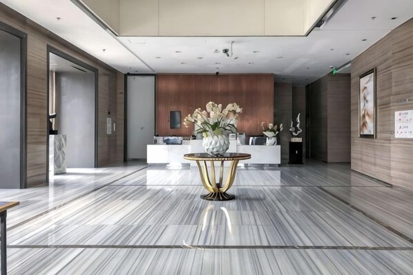 A hotel lobby with a reception desk, a marble floor, and a decorative table with flowers.