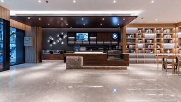 Un área de recepción moderna con piso de mármol, mostrador de madera y una estantería llena de libros.