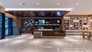 Uma área de recepção moderna com piso de mármore, balcão de atendimento, painel digital e estante de livros.