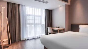 A hotel room with a bed, a desk, a chair, and a window with curtains.