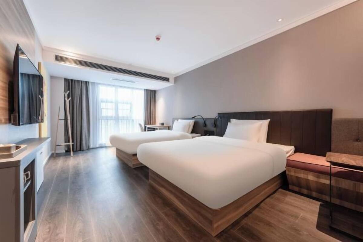 Ein modernes Hotelzimmer mit einem großen Bett, einem Nachttisch, einem Fernseher und einem Fenster mit Vorhängen.