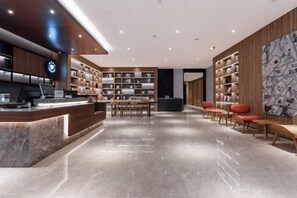 A modern hotel lobby with a reception desk, seating area, and bookshelves. - HanTing Hotel (Dujiangyan) (Dujiangyan)