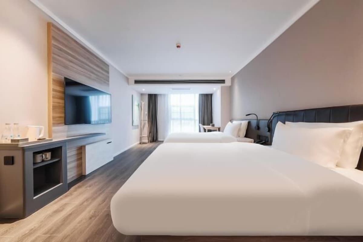 A hotel room with a large bed, a desk, a flat-screen TV, and a window with curtains.
