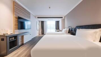 A hotel room with a large bed, a desk, a flat-screen TV, and a window with curtains.
