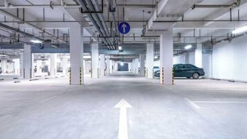 Un estacionamiento subterráneo con flechas direccionales en el suelo, pilares de hormigón y un letrero azul colgante.