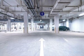 An underground parking garage with directional arrows on the floor, concrete pillars, and a blue overhead sign. - HanTing Hotel (Dujiangyan) (Dujiangyan)