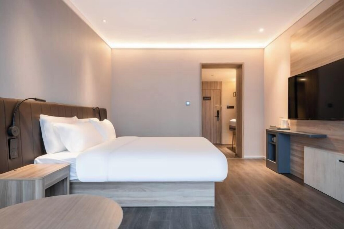 A modern hotel room with a large bed, bedside table, and a TV.