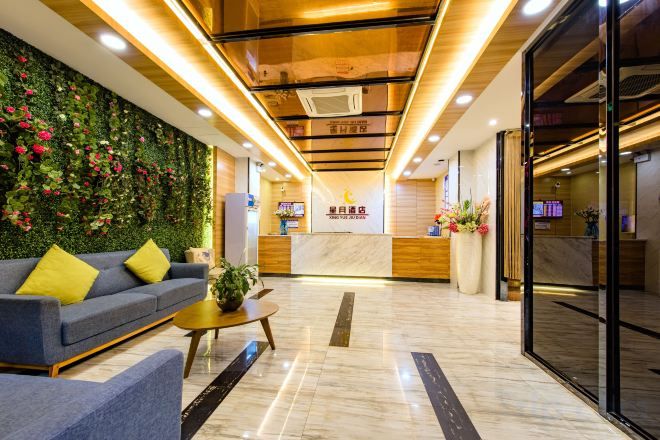 Un hall de hotel con una recepción, un sofá, una mesa de centro y una pared verde con flores.
