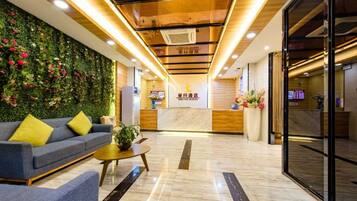 Un hall de hotel con una recepción, un sofá, una mesa de centro y una pared verde con flores.