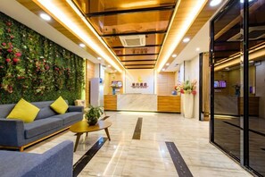 A hotel lobby with a reception desk, a sofa, a coffee table, and a green wall with flowers. - Xingyue Hotel (Jiangnan Bus Terminal Dashatian Subway Station) (Nanning)