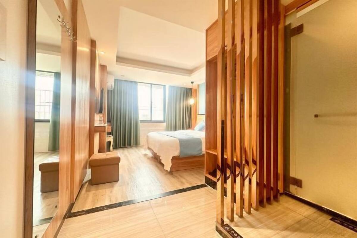 Una habitación de hotel con cama, zona de estar, un separador de madera y una puerta.