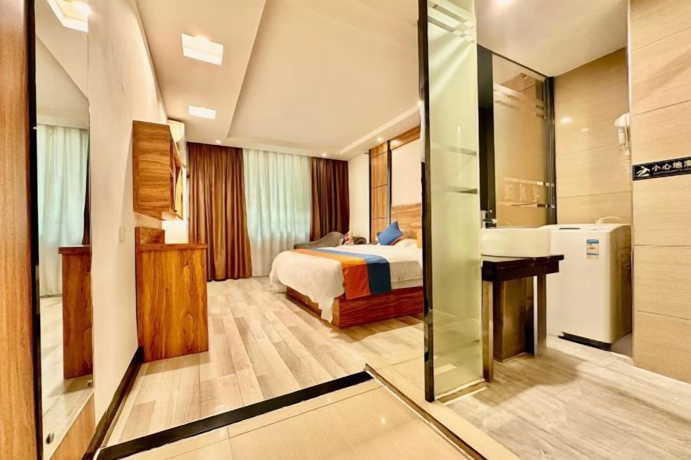 Habitación de hotel con cama, escritorio, espejo, lavabo y separador de vidrio.