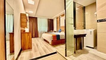 Habitación de hotel con cama, escritorio, espejo, lavabo y separador de vidrio.