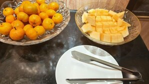 Two glass bowls on a countertop, one filled with oranges and the other with cubed fruit, possibly mango. A white plate with a knife rests beside them. - Xingyue Hotel (Jiangnan Bus Terminal Dashatian Subway Station) (Nanning)