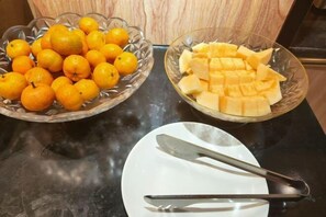 Two glass bowls on a countertop, one filled with oranges and the other with cubed fruit, possibly mango. A white plate with a knife rests beside them. - Xingyue Hotel (Jiangnan Bus Terminal Dashatian Subway Station) (Nanning)