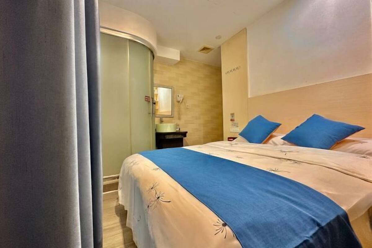 Una habitación de hotel con una cama, una mesita de noche, un espejo y una lámpara en la pared.