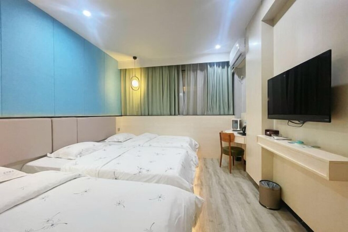 A hotel room with two beds, a desk with a chair, a television, and a window with curtains.