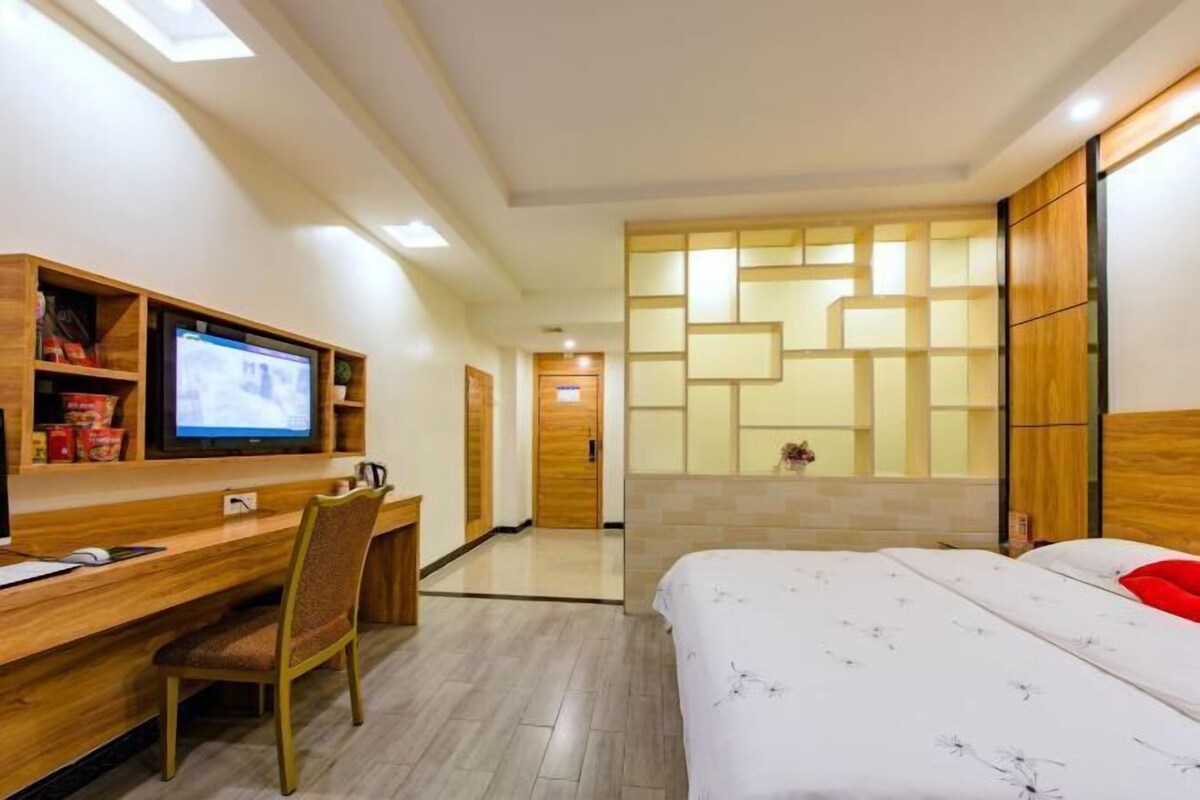 A hotel room with a bed, a desk with a computer, a TV, and a wooden cabinet.