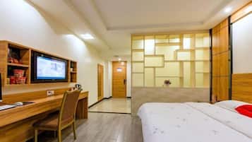 Habitación de hotel con cama, escritorio con computadora, televisión y un armario de madera.