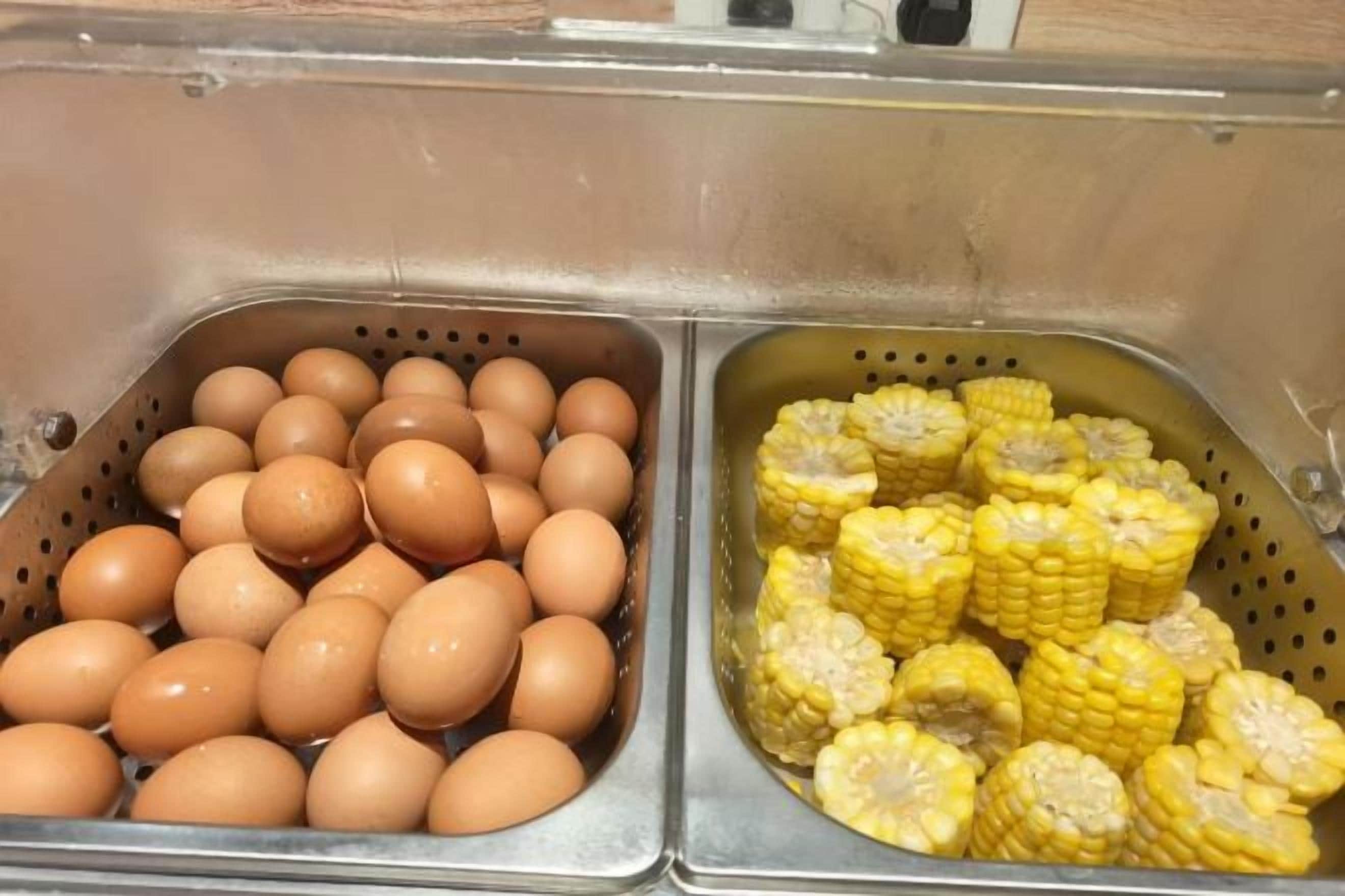 Un lavamanos de acero inoxidable con dos compartimentos, uno con huevos y el otro con mazorcas de maíz.