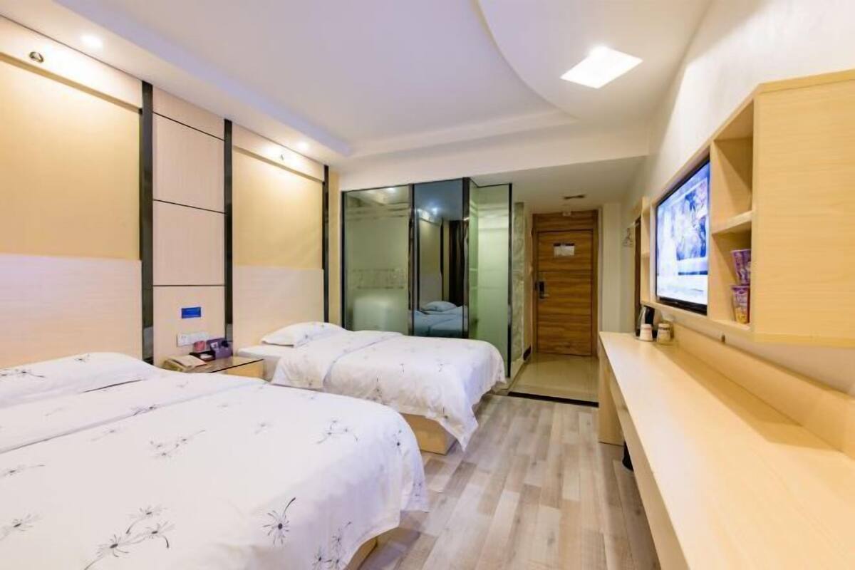 Habitación de hotel con dos camas, un banco de madera, un televisor y un pequeño escritorio.