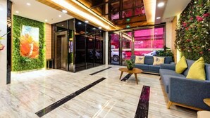 Eine Lobby mit Marmorboden, einem blauen Sofa, einer grünen Wand mit einer Pflanze und einer Glastür zu einem Auto.