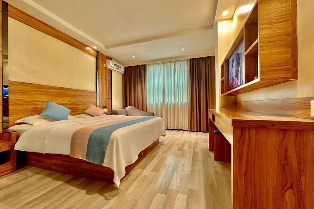 Habitación de hotel con una cama de madera, televisión, escritorio y ventana con cortinas.
