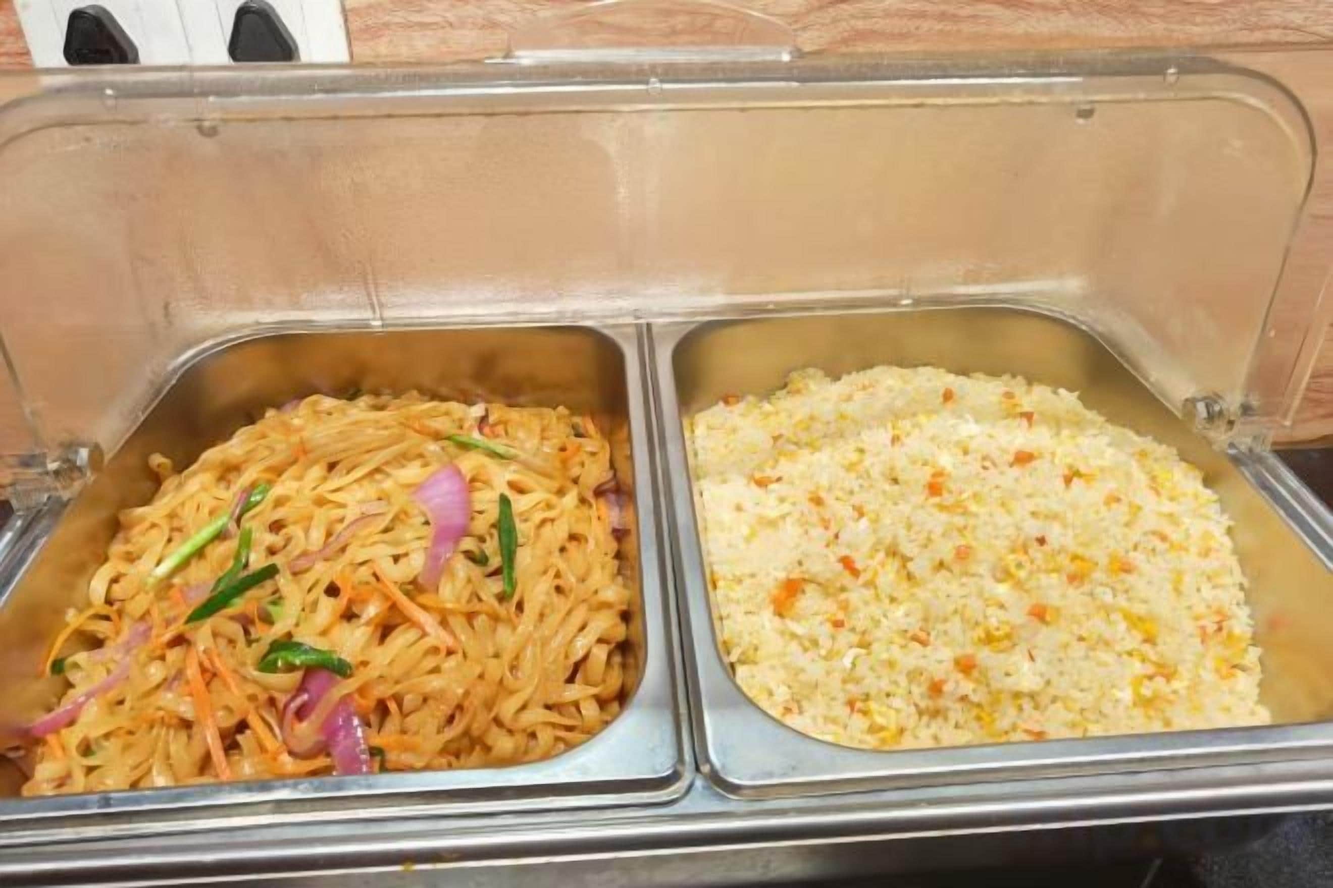 A buffet with two metal serving trays, one containing noodles with vegetables and the other containing rice with vegetables.