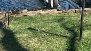 A lakeside park with a wooden dock, a lamp post, and a grassy area.