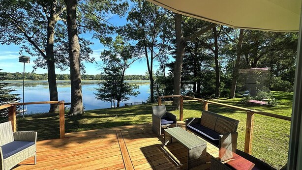 A wooden deck with wicker furniture overlooking a lake, surrounded by trees.