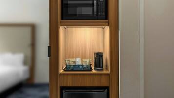 A compact kitchenette with a microwave, coffee maker, and storage for coffee pods.